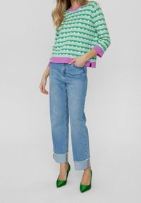 Pull en maille rayé vert et blanc avec bordure violette, associé à un jean taille haute bleu clair avec ourlets retroussés et des escarpins verts à bout pointu.