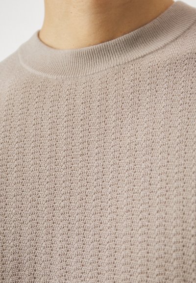 Ανοιχτό μπεζ πλεκτό πουλόβερ με υφή, διακοσμημένη επιφάνεια και στρογγυλή λαιμόκοψη. Περιλαμβάνει ριμπά στοιχεία στο γιακά.