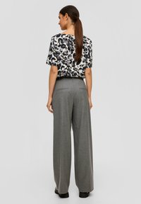 Bluse mit Leopardenmuster und kurzen Ärmeln, kombiniert mit hochtaillierten, weit geschnittenen grauen Hosen, die eine glatte Textur und klare Linien aufweisen.
