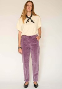 Pantalons en velours côtelé lavande avec une coupe décontractée et des poches avant, associés à un haut crème à manches courtes et une écharpe noire. Escarpins noirs.