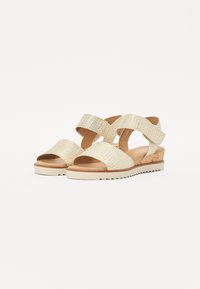 Gold woven sandals with a cork accent, featuring wide straps and a rubber sole. Open-toe design and a low wedge heel.
