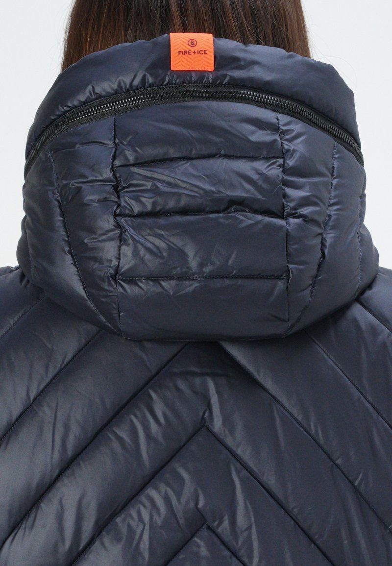 Marineblaue Steppjacke mit einem gesteppten Design, hohem Kragen mit einem orangefarbenen Etikett und einem Reißverschluss entlang des Halsausschnitts für zusätzliche Wärme.