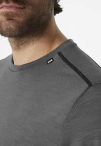 Grijze gebreide trui met een ronde hals, voorzien van een gestructureerde stof, zwarte accentstiksels op de schouder en een klein logo-label bij de kraag.