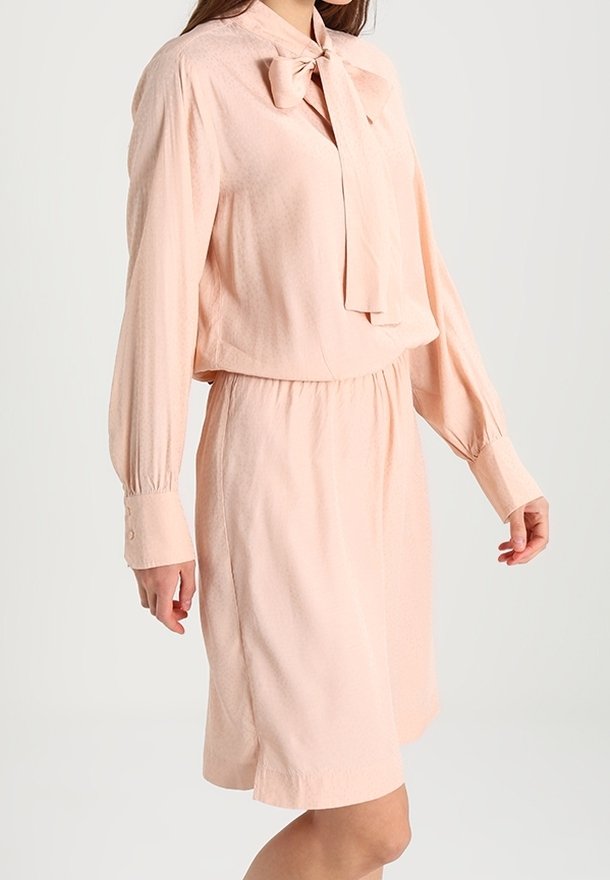 Růžovo-oranžové šaty s límcem na mašli, dlouhými rukávy, elastickým pasem a texturovanou látkou. Obsahují manžety na knoflíky a volný střih.