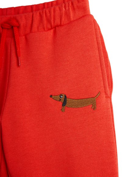 Pantaloni della tuta rossi con vita a coste e cordino, dotati di un design di un bassotto marrone ricamato sulla coscia sinistra.