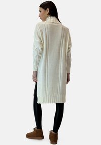 Kremhvid kabelstrikket sweaterkjole med høj krave, tilspidsede ærmer og ribkant nederst. Kombineret med sorte leggings og brune ankelstøvler.