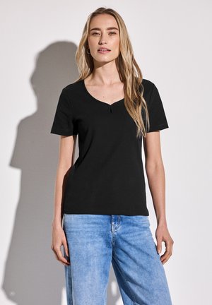 Top corto de manga corta negro con textura acanalada, escote en V y detalle de ojal, combinado con jeans de mezclilla azul claro. Textura suave, diseño casual.