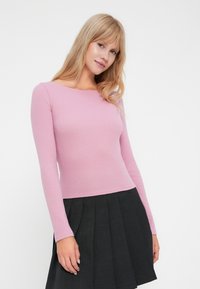 Langermet tettsittende topp i myk rosa ribbet stoff, med båt-hals, sammen med en plissert svart skjørt for kontrast.
