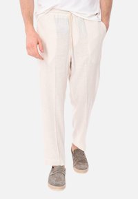 Pantaloni in lino beige chiaro con vita elasticizzata e cordoncino, dotati di due tasche laterali e un fit rilassato che si restringe alla caviglia.