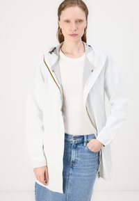 Lahka bela jakna s kapuco, z srebrno notranjo oblogo, sprednjim zadrgo in elastičnimi manšeti, v kombinaciji z bež zgornjim delom in denim krilom.
