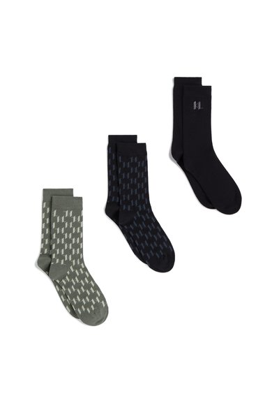 Trois paires de chaussettes mi-mollet en vert olive, noir avec motif bleu, et noir uni avec un petit logo sur la cheville, présentées sur fond blanc.