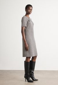 Robe à manches courtes, longueur genou, avec un motif texturé noir et blanc, portée avec des bottes noires à talons aiguilles montant jusqu'au genou. Design simple, coupe droite.