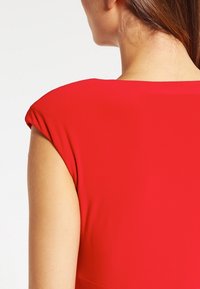 Vestido rojo con una tela suave y texturizada, con un escote amplio y mangas cortas, mostrado desde la parte posterior enfocándose en los detalles de los hombros.