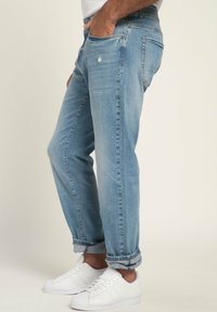 Vaqueros de mezclilla azul claro con un corte relajado, que presentan detalles desgastados y puños doblados, combinados con zapatillas blancas.