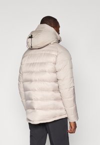 Jachetă puffer bej cu guler înalt și glugă ajustabilă, având un model matlasat orizontal și o textură moale și fină.