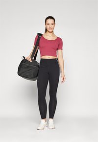Rød crop-top, svarte leggings med stripene på sidene, og hvite sneakers. Svart veske med teksturert og glatt finish, båret over skulderen.