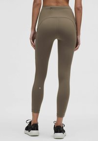 Leggings a vita alta e aderenti in materiale khaki con una superficie liscia. Presentano una tasca posteriore e il logo nella parte inferiore della gamba.