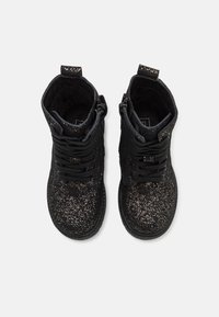 Černé boty s jemnou třpytivou texturou, mají šněrování, zipy po stranách a kulatou špičku. Měkké podšívka viditelná uvnitř.