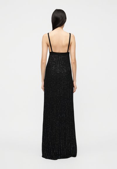 Μαύρο φόρεμα μήκους μέχρι το πάτωμα με λεπτές τιράντες, με υφή κάθετων ριγών και διακριτική λάμψη σε όλο του το μήκος, σχεδιασμός με ανοιχτή πλάτη.