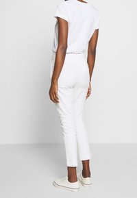 Vita bomullsblandade byxor med smal passform, avkortad fåll, bälteshällor och sid- samt bakfickor, kombinerade med vita sneakers.