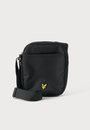 Must väike risti kott reguleeritava rihmaga ja kollase kotka logoga ees, ühtlase heleda tausta taustal.