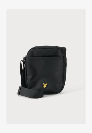 Zwarte kleine crossbodytas met verstelbare riem en geel adelaar logo aan de voorkant, tegen een effen lichte achtergrond.