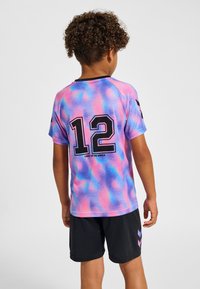 Kortärmad, flerfärgad tröja med rosa, lila och blå abstrakta mönster, med siffran 12 och texten "LIGHT UP THE WORLD". Svarta shorts.