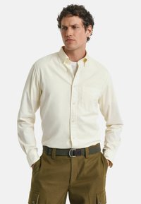 Hellgelbes langärmliges Button-Down-Hemd mit einer Brusttasche, kombiniert mit olivgrünen Cargo-Hosen. Baumwollmaterial mit glatter Textur.