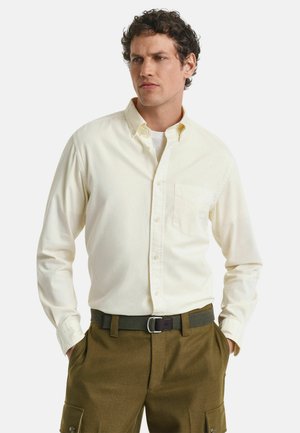 Chemise à manches longues jaune clair à boutons avec une poche poitrine, associée à un pantalon cargo vert olive. Matière en coton avec une texture lisse.
