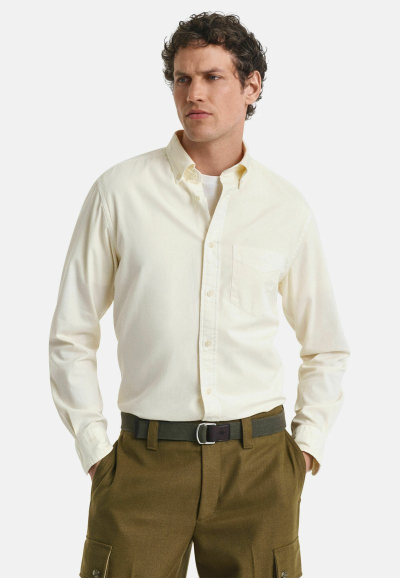 Hellgelbes langärmliges Button-Down-Hemd mit einer Brusttasche, kombiniert mit olivgrünen Cargo-Hosen. Baumwollmaterial mit glatter Textur.