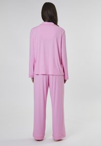 Rosa loungekläder som består av en långärmad topp med krage och lösa byxor. Mjukt material med en slät yta och avslappnad design.