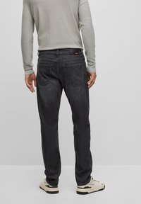 Mörkgrå denimjeans med rak skärning, utrustade med en logotypmärke och subtila sömmar på bakfickan. Matchas med en ljus tröja och skor.