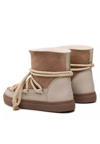 Beige high-top sneakers hebben een zacht suède bovenwerk, een gevoerde enkelband en gevlochten veters. Getextureerde rubberen buitenzool met branding op de hiel.