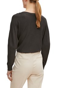 Pull à manches longues gris foncé, col côtelé, coupe décontractée, assorti à un pantalon beige clair sur mesure, stylisé avec des plis au dos et des poches.