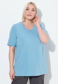 T-shirt azzurro chiaro a maniche corte con scollatura rotonda e vestibilità rilassata, realizzato in tessuto morbido; indossato con pantaloni grigi.