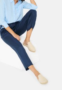 Beige espadrilky na slip-on s měkkým semišovým svrškem a jutu podrážkou, v kombinaci s námořnickými kalhotami a světle modrou lněnou košilí.