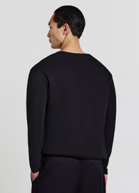 Maglione nero a maniche lunghe con un motivo strutturato a coste e scollo rotondo, visto da dietro. Il materiale sembra morbido e leggero.