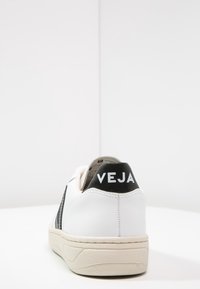 Valkoinen nahkakenkä mustalla heel tabilla, jossa on "VEJA" -logo. Harmaa teksturoitu sivupaneeli, kerma sole, pyöreä kärki ja minimalistic design.
