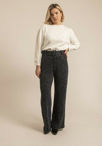 Haut à manches longues blanc avec une texture côtelée, associé à un pantalon à taille haute à carreaux avec des jambes larges en bleu marine et noir. Chaussures à talons noires.