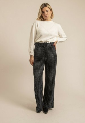 Haut à manches longues blanc avec une texture côtelée, associé à un pantalon à taille haute à carreaux avec des jambes larges en bleu marine et noir. Chaussures à talons noires.