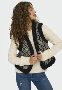 Zwart-wit gestreepte vest met een gezellige, textuurstof over een crèmekleurige trui, met geribde manchetten en een comfortabele pasvorm.
