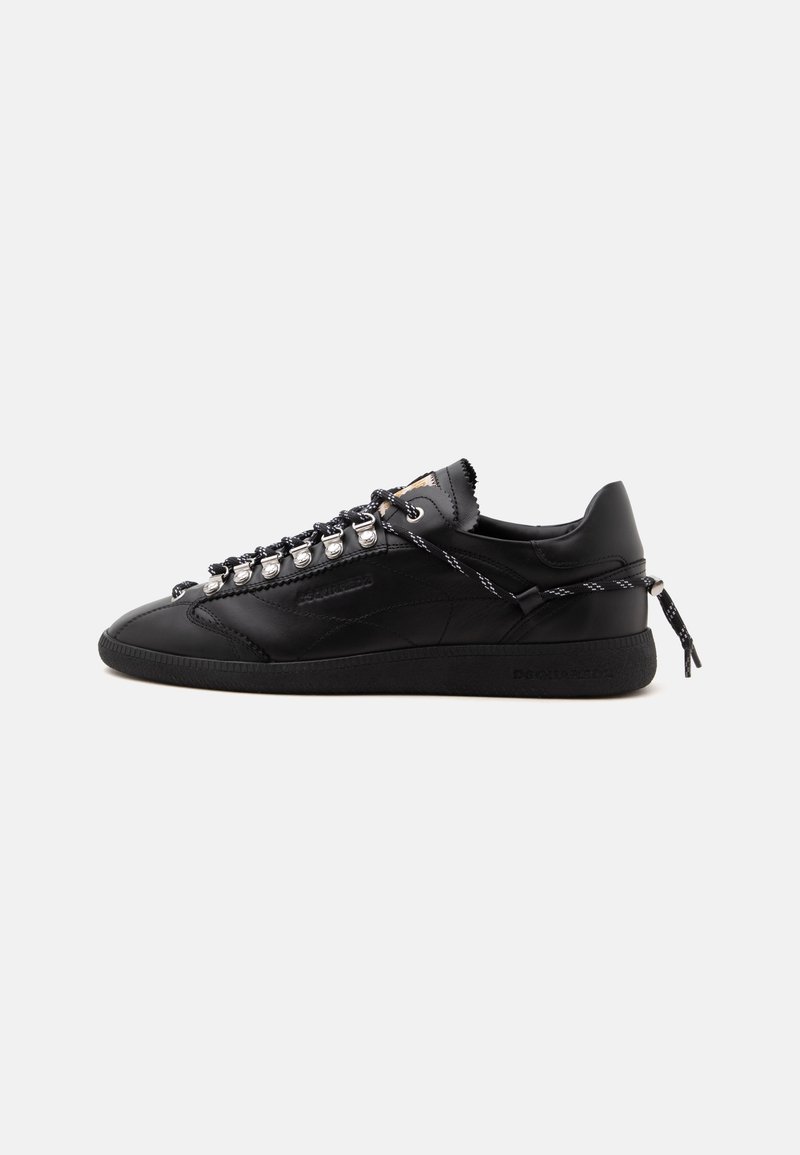 Μαύρο χαμηλό sneaker με χοντρή σόλα, ασημένιες τρύπες για κορδόνια, μαύρα και λευκά κορδόνια δεμένα στη φτέρνα και διακριτικό ανάγλυφο λογότυπο στο πλάι.
