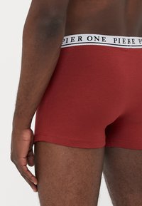 Rote Boxer-Briefs mit einer enganliegenden Passform, aus weichem Stoff gefertigt. Mit einem weißen Bund, auf dem "PIER ONE" in Schwarz gedruckt ist.