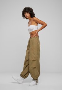 Beige baggy bukser med elastisk talje, snøre detaljer og flere lommer, parret med hvide sneakers på en neutral baggrund.