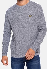 Grauer Pullover mit langen Ärmeln und strukturiertem Strickdesign. Verfügt über ein dezentes gelbes Logo auf der Brust sowie gerippte Bündchen und Saum.
