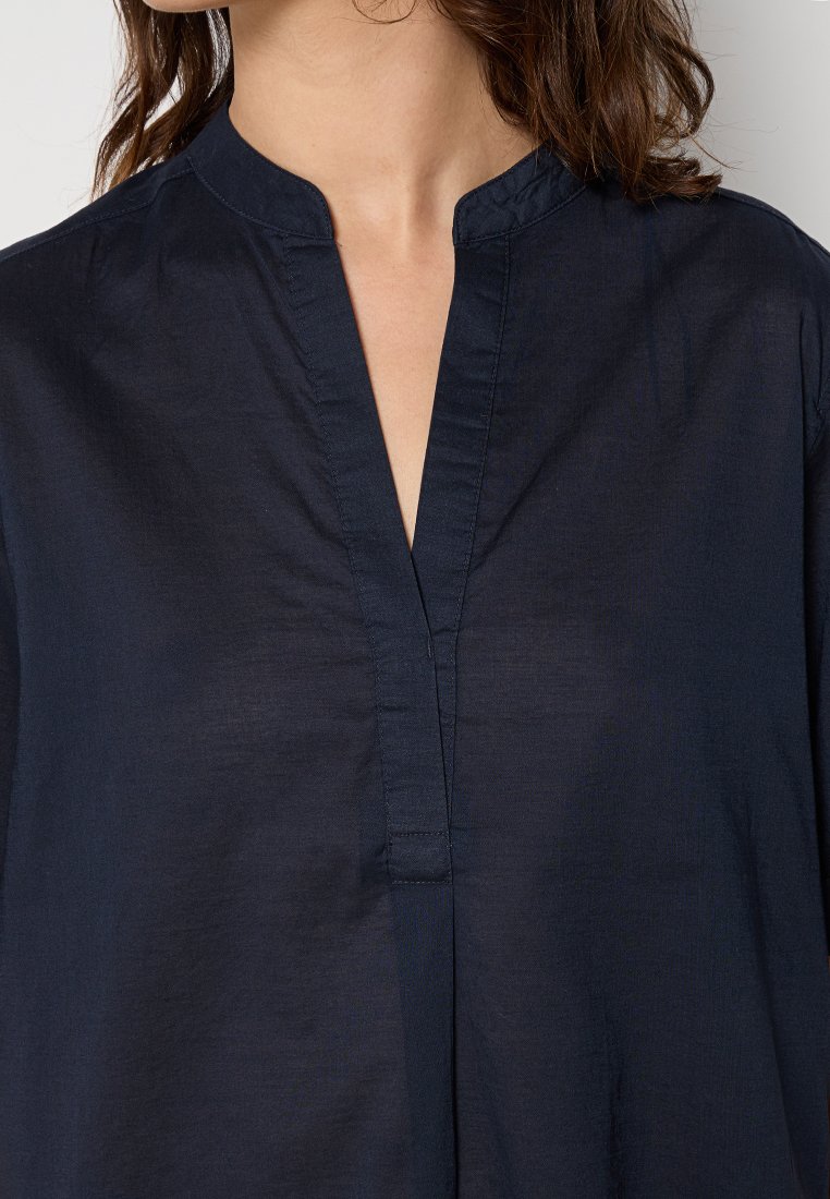 Marineblaue, leichte Baumwoll-Tunika mit Stehkragen und einer teilweisen Knopfleiste. Glatte Textur, lockerer Schnitt mit seitlichen Schlitzen.