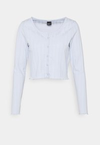 Světle modrý zkrácený kardigan vyrobený z žebrované látky. Má dlouhé rukávy, kulatý výstřih a zapínání na knoflíky v přední části.