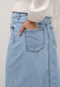 Falda de mezclilla azul claro con un bolsillo trasero y costuras en contraste. La tela tiene una textura suave y un acabado ligeramente desgastado.