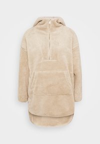 Beżowy oversize'owy sweter z wysokim kołnierzem, zapięciem na pół zamek, dużą kieszenią z przodu oraz miękkim, teksturowanym materiałem polarowym.