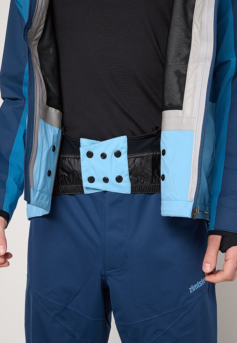 Kurtka odporna na wodę w kolorze niebieskim i szarym z zapięciem na zatrzaski w talii. Posiada czarny elastyczny pas oraz podszewkę z siateczki.